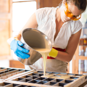 woman pouring soap contents into soap mold while wearing safety goggles