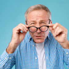A man squinting while holding eyeglasses.